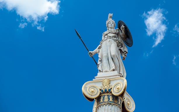 Statue of Goddess Athina holding spear and shield against blue sky.