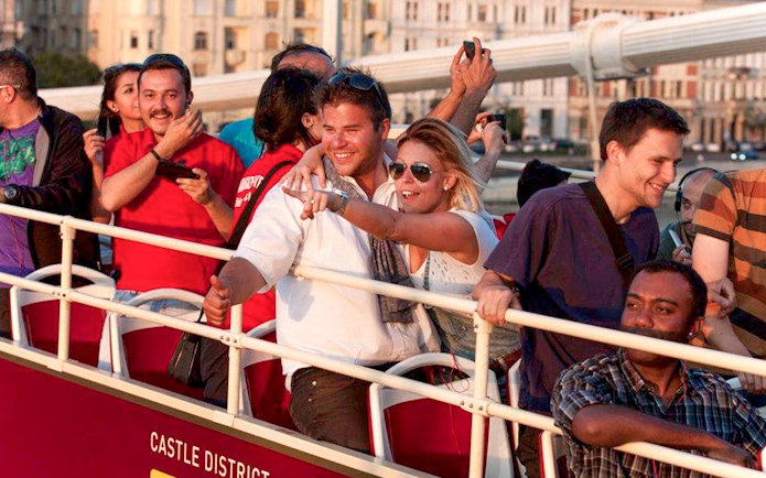 Tourists enjoying Budapest Big Bus tour near Hungarian Parliament and Danube River.