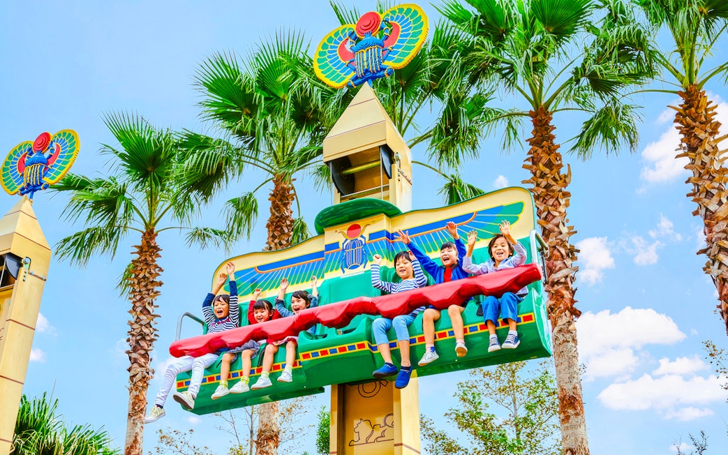 Children enjoying a ride at Legoland Japan with palm trees in the background.