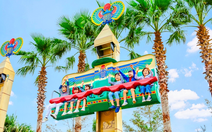 Children enjoying a ride at Legoland Japan with palm trees in the background.