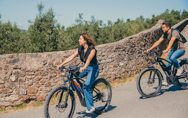 Cyclists on e-bikes riding along a stone wall in Florence hills.