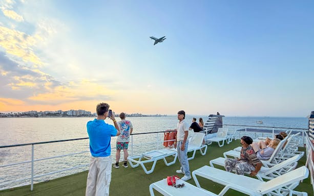 Sunset cruise from Larnaca with people on deck watching a plane fly overhead.