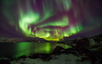 Northern Lights over snowy landscape and water in Norway.