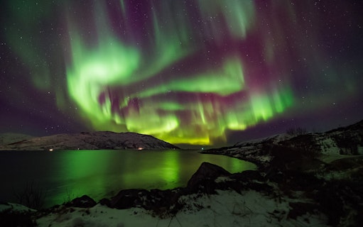 Northern Lights over snowy landscape and water in Norway.
