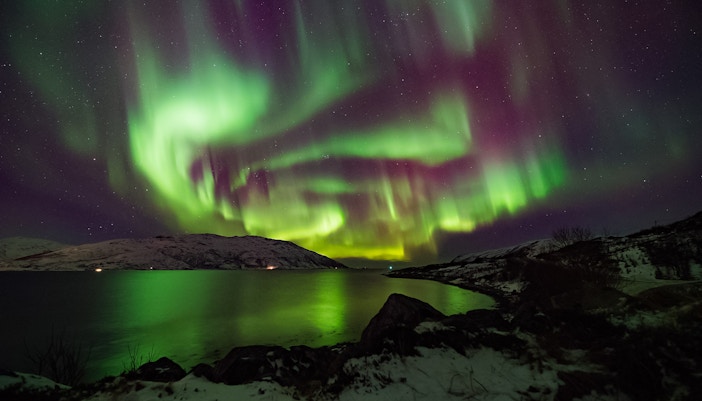 Northern Lights over snowy landscape and water.