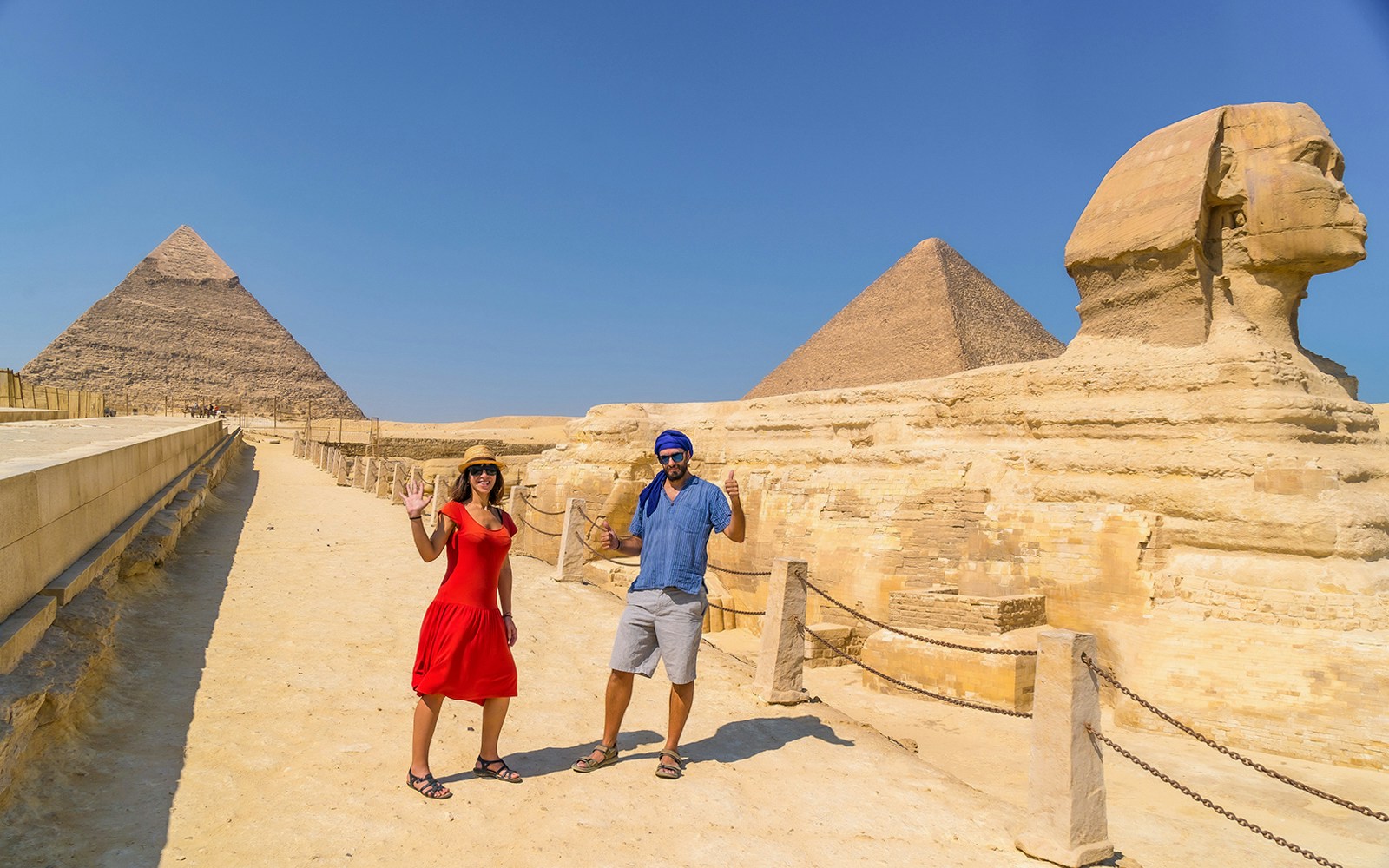Tourist couple posing at The Great Sphinx of Giza with pyramids in the background.