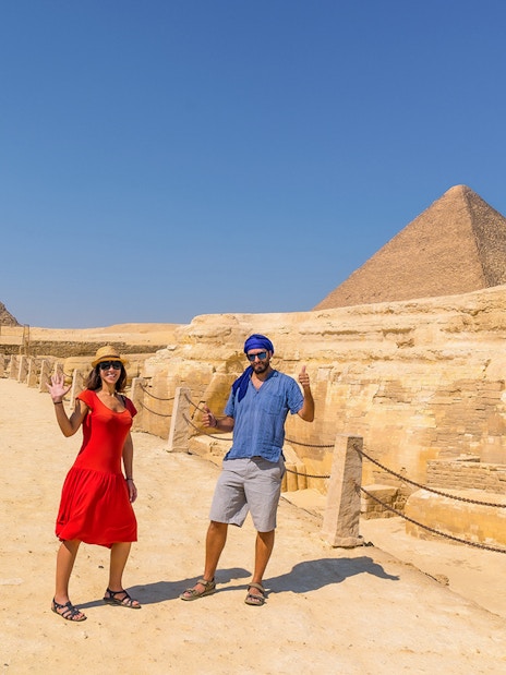 Tourist couple posing at The Great Sphinx of Giza with pyramids in the background.