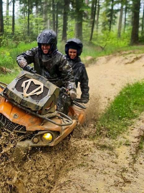 Visitors riding a quad bike through muddy forest trail in Zakopane.