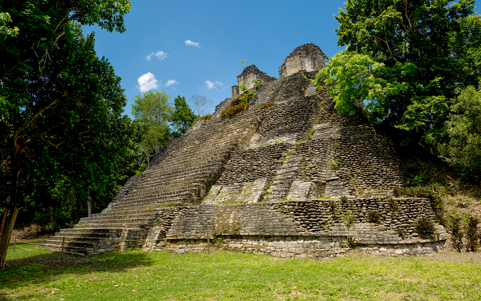 Stone pyramid structure surrounded by lush greenery at Temple of the Owls near Chichen Itza.