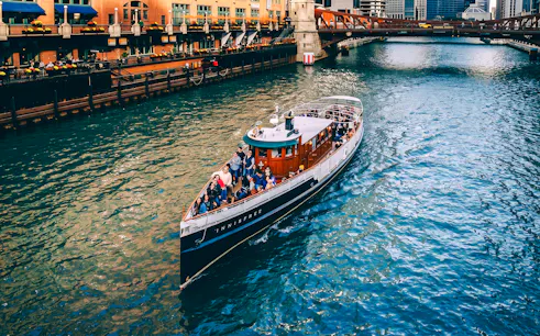 Cruise boat on Chicago River passing under a bridge with city buildings in view.