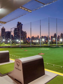 Top Golf driving range with city skyline at dusk.