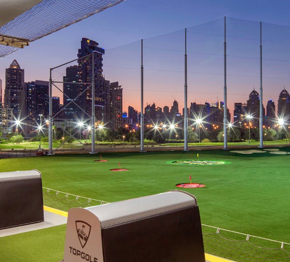 Top Golf driving range with city skyline at dusk.