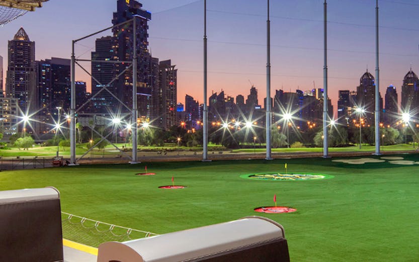 Top Golf driving range with city skyline at dusk.