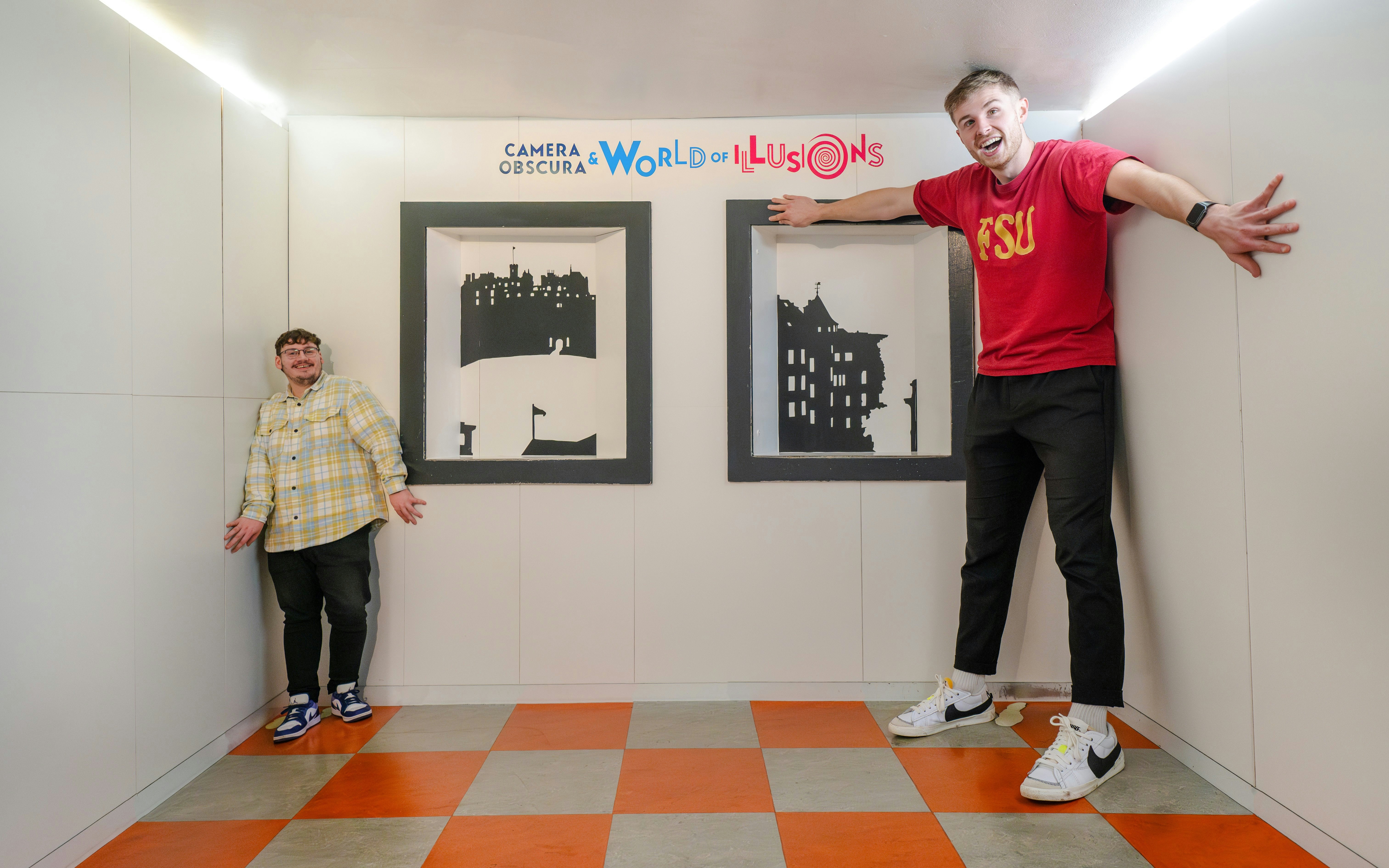 Two people in the Ames Room at Camera Obscura & World of Illusions, Edinburgh, creating an optical illusion.