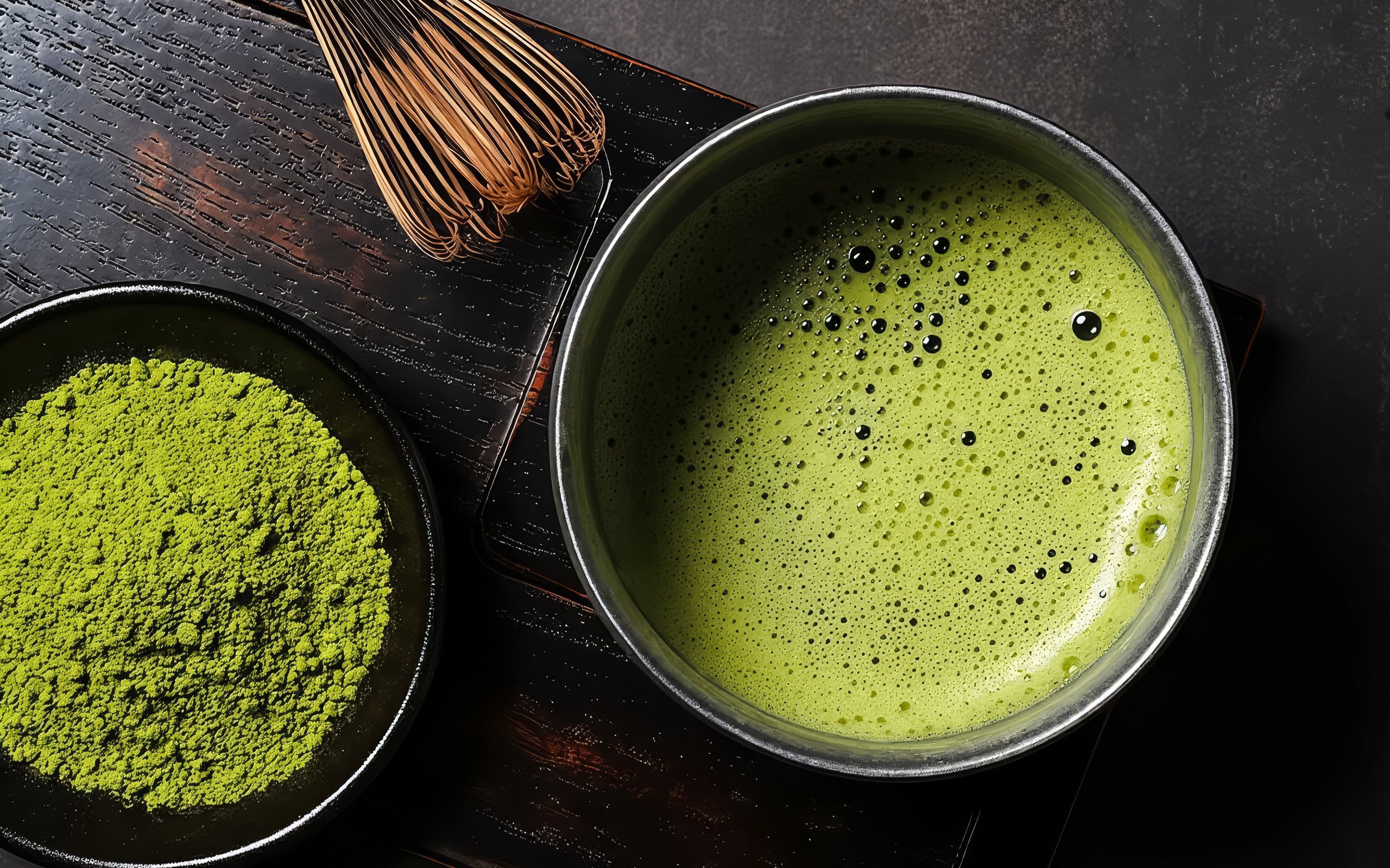 Close-up of matcha powder and whisk next to a bowl of frothy matcha tea.