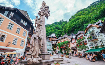Central square in Hallstatt with historic buildings and a statue, surrounded by lush hills.