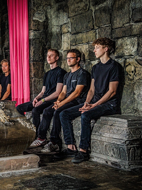 Guide in historical costume leading a tour inside Berlin Dungeon with visitors seated around a tomb.