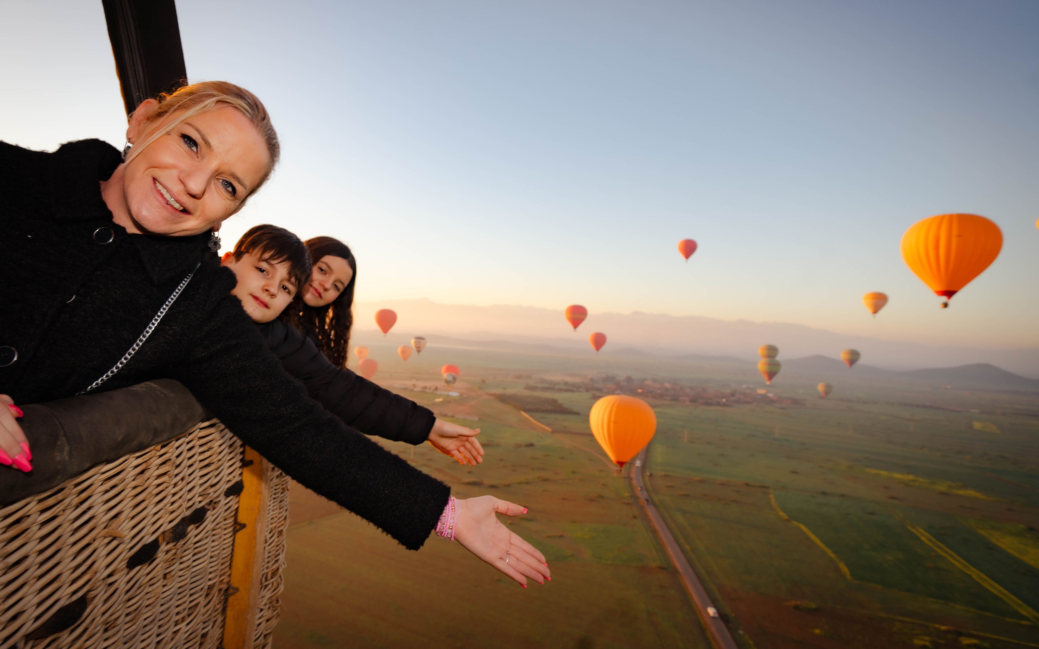 Friends enjoying a hot air balloon flight over Marrakech landscape.