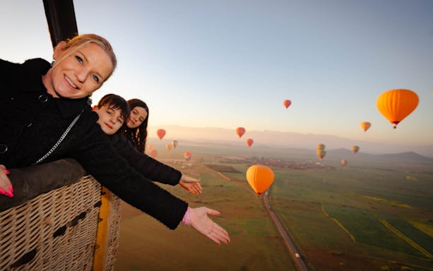 Friends enjoying a hot air balloon flight over Marrakech landscape.
