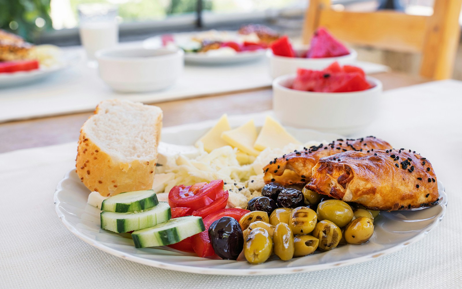 Traditional breakfast with olives, cheese, bread, cucumbers, and pastries on a plate.
