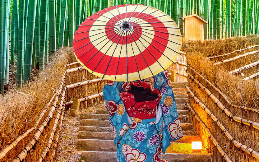 Person in kimono with umbrella walking through Arashiyama Bamboo Grove, Kyoto.