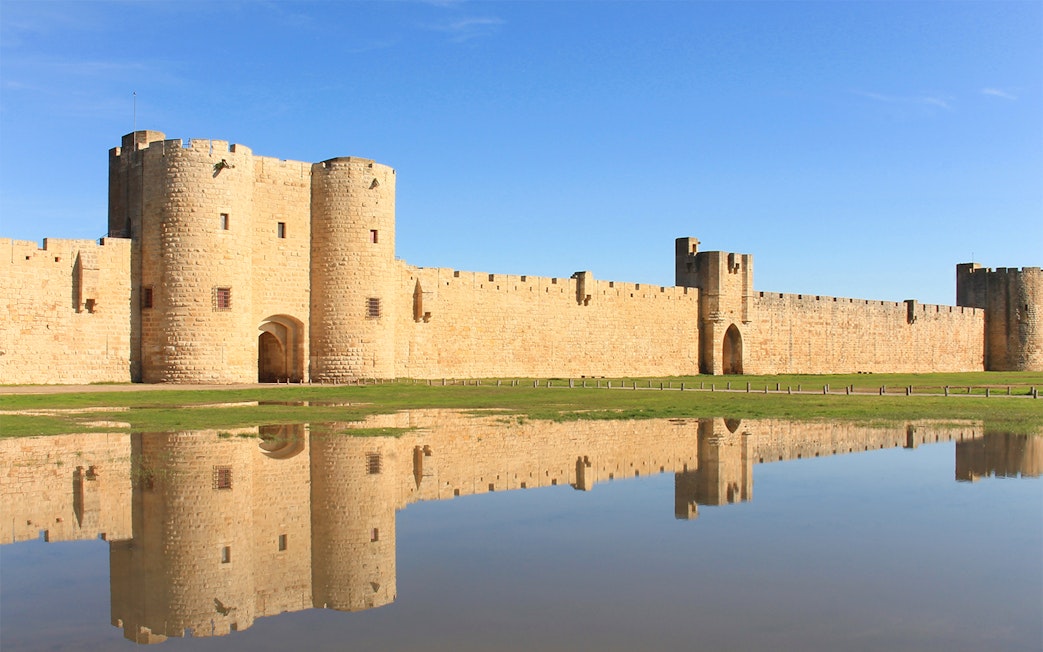 Towers and ramparts of Aigues-Mortes reflected in water, France.