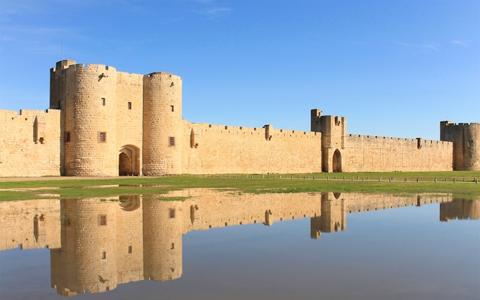 Towers and ramparts of Aigues-Mortes reflected in water, France.