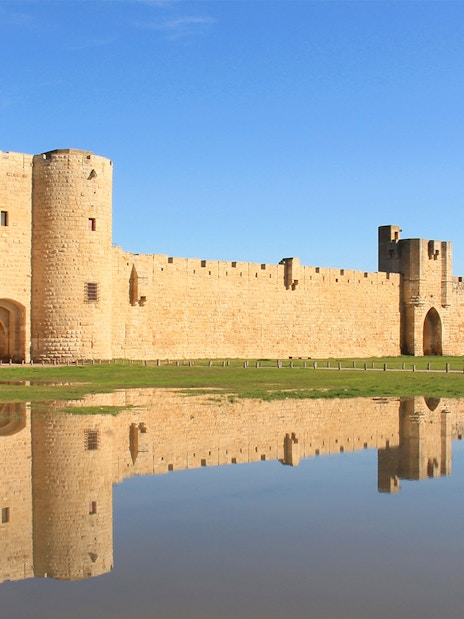 Towers and ramparts of Aigues-Mortes reflected in water, France.