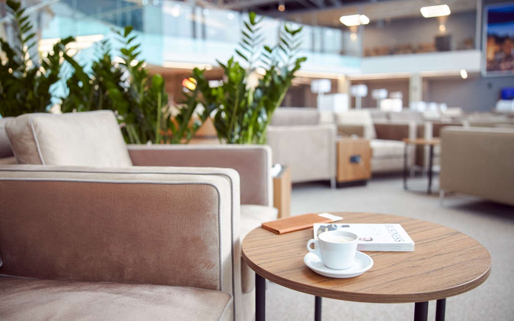 Cozy airport lounge with armchairs, coffee table, and plants.