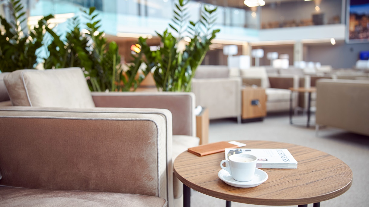 Cozy airport lounge with armchairs, coffee table, and plants.