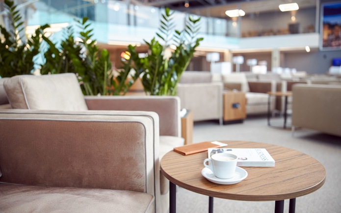 Cozy airport lounge with armchairs, coffee table, and plants.