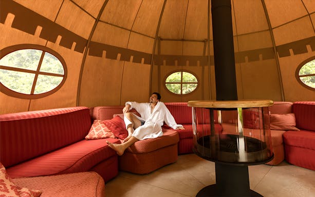 Man relaxing in a robe inside a cozy lounge at QC Terme Roma.