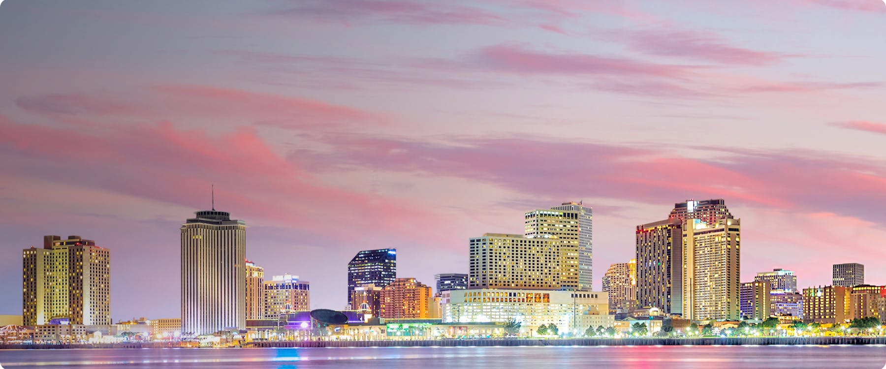 New Orleans skyline at sunset with illuminated buildings along the waterfront.