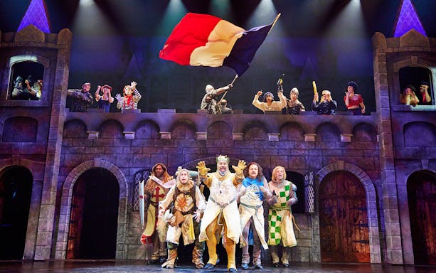 Knights performing in Spamalot musical with castle backdrop and French flag.