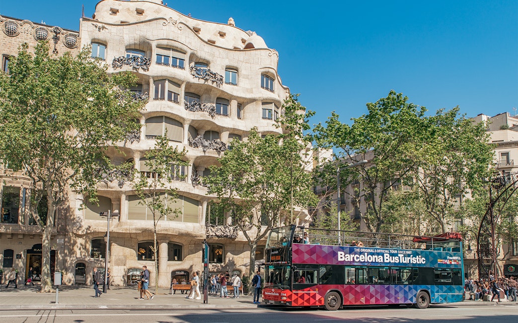 Barcelona tour bus in front of Casa Milà on a sunny day.