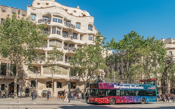 Barcelona tour bus in front of Casa Milà on a sunny day.
