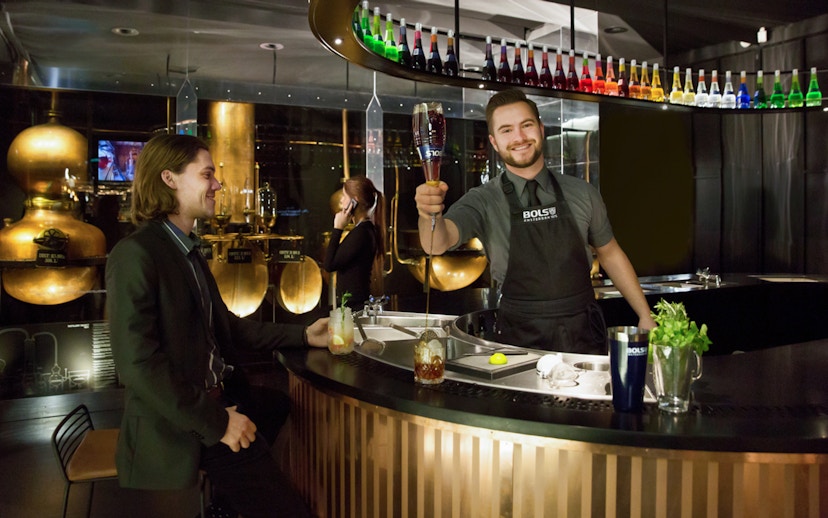 Bartender serving a cocktail at House of Bols in Amsterdam, with colorful bottles displayed above.