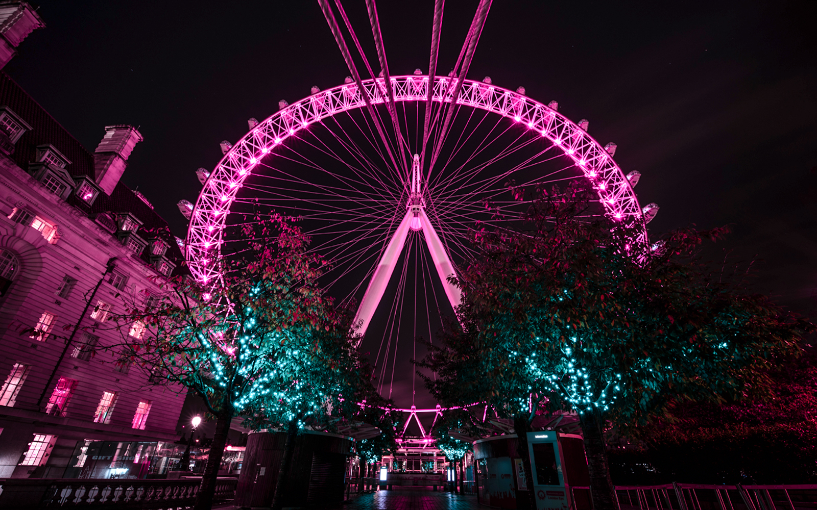 London Eye illuminated at night with nearby building and trees.