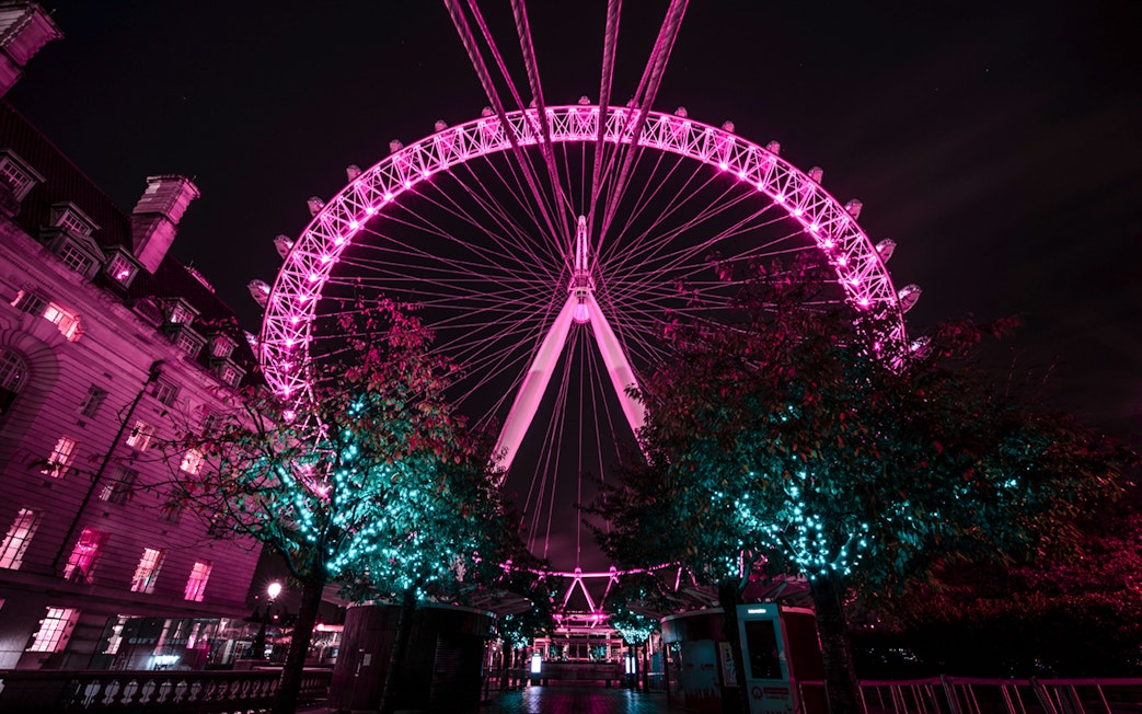 London Eye illuminated at night with nearby building and trees.