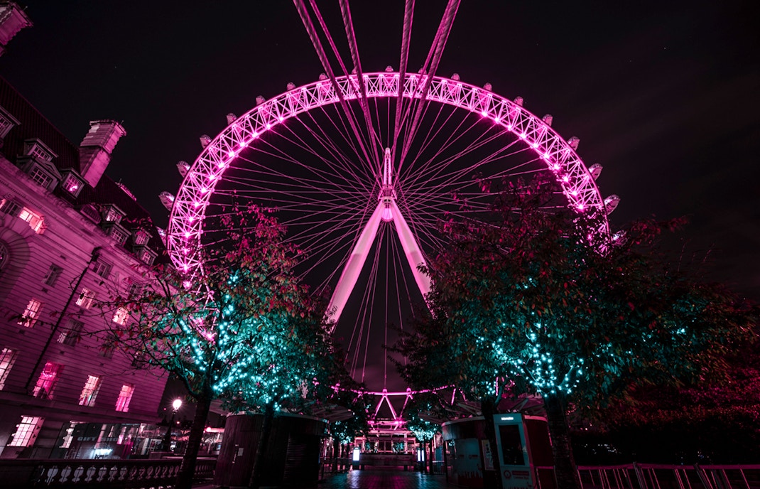 London Eye illuminated at night with nearby building and trees.