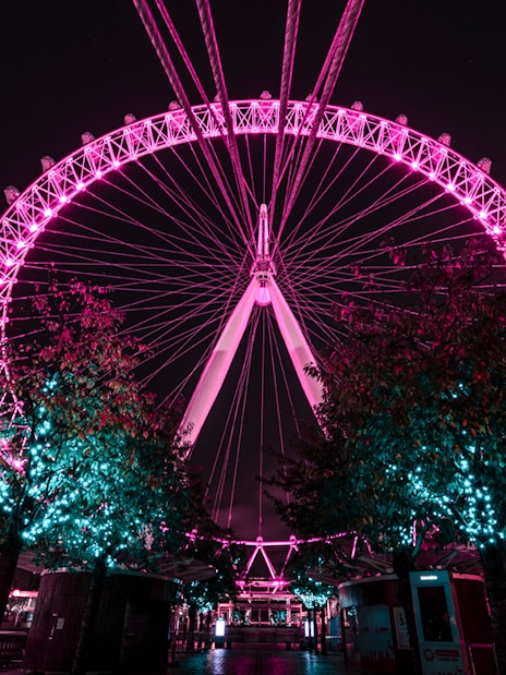 London Eye illuminated at night with nearby building and trees.