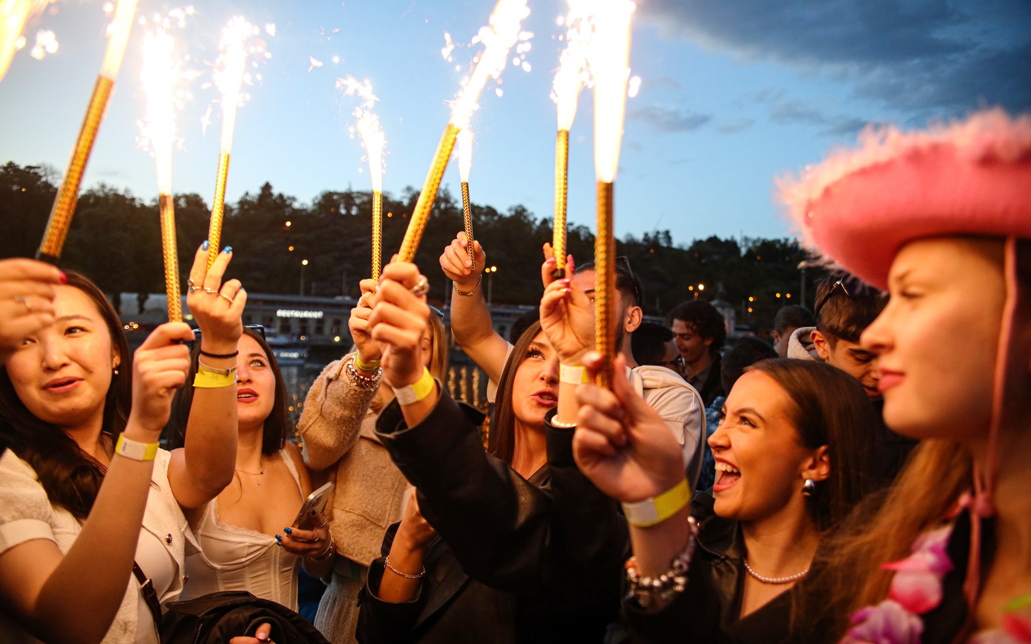 Group celebrating on a boat cruise with sparklers at dusk.