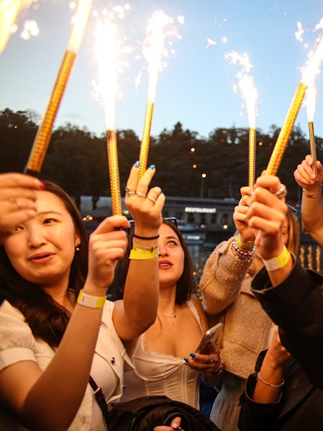 Group celebrating on a boat cruise with sparklers at dusk.