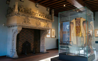 Gruuthusemuseum interior with ornate fireplace and historical garment display.