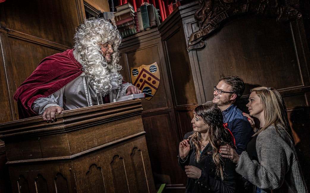 Judge in period costume engaging with visitors at York Dungeon courtroom.