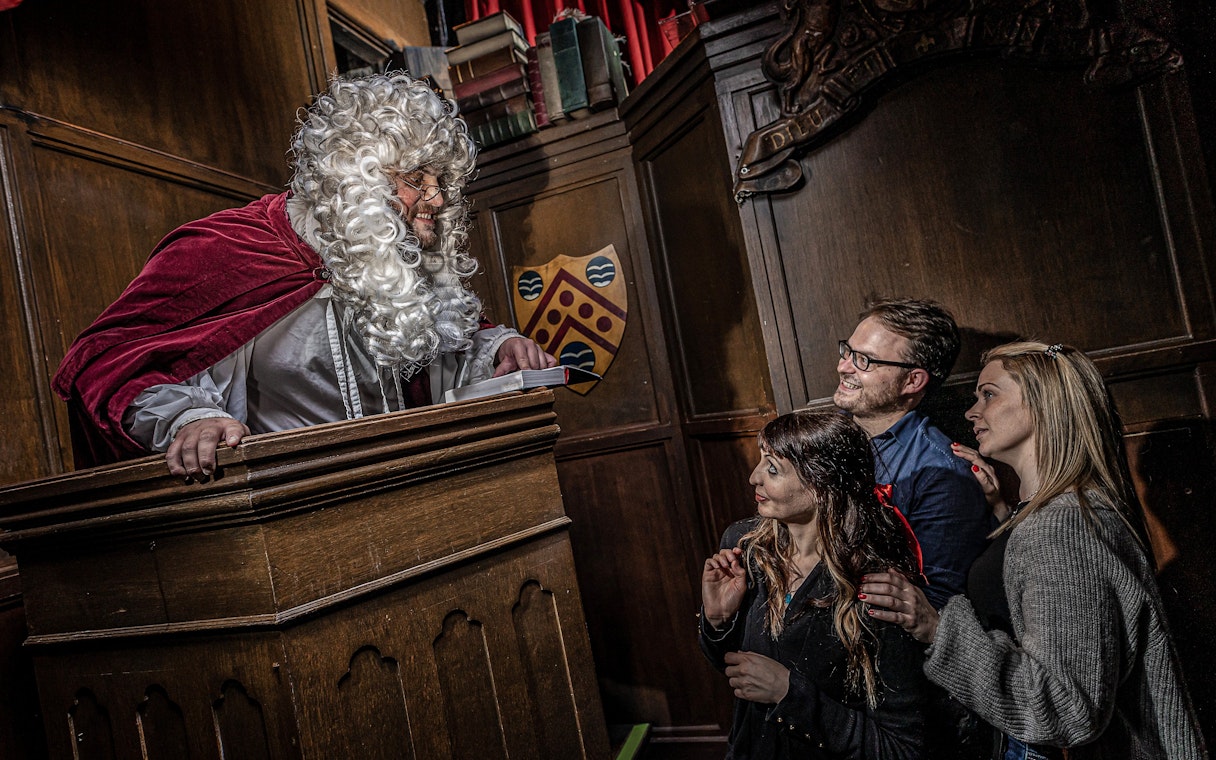 Judge in period costume engaging with visitors at York Dungeon courtroom.