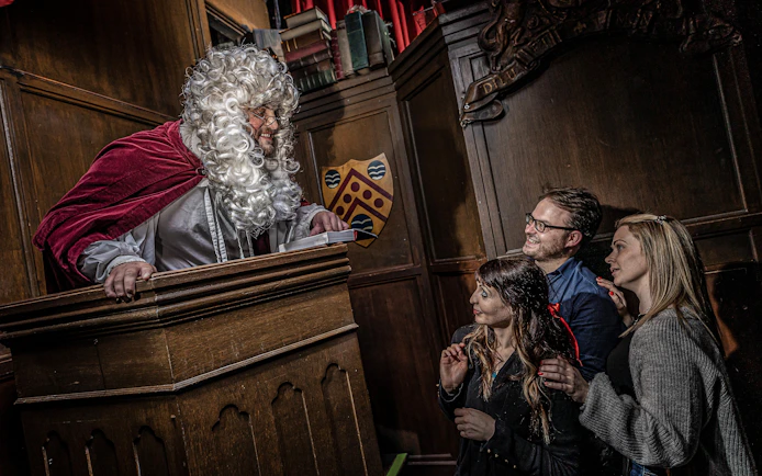 Judge in period costume engaging with visitors at York Dungeon courtroom.