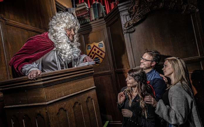 Judge in period costume engaging with visitors at York Dungeon courtroom.