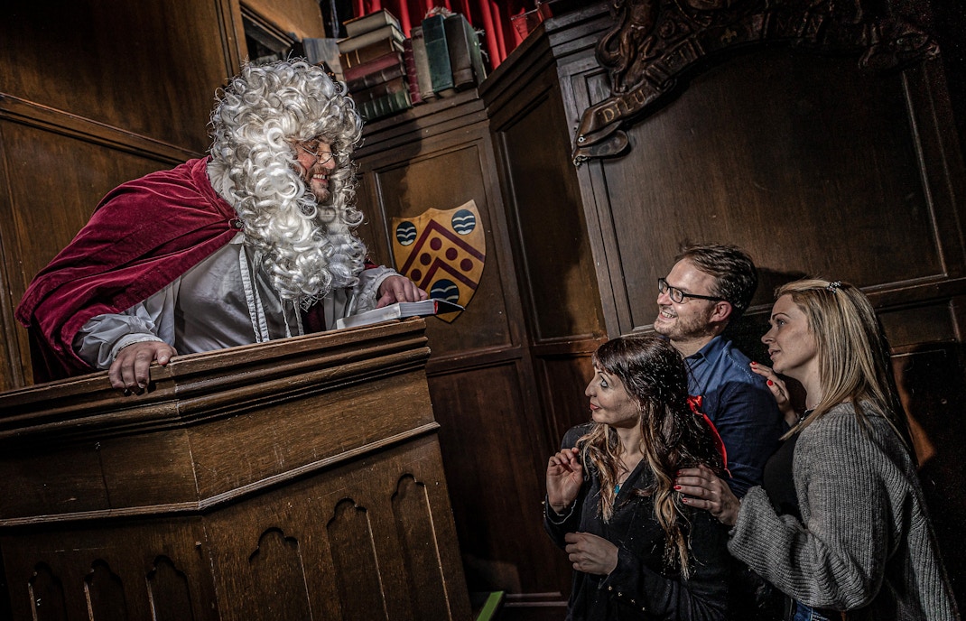 Judge in period costume engaging with visitors at York Dungeon courtroom.