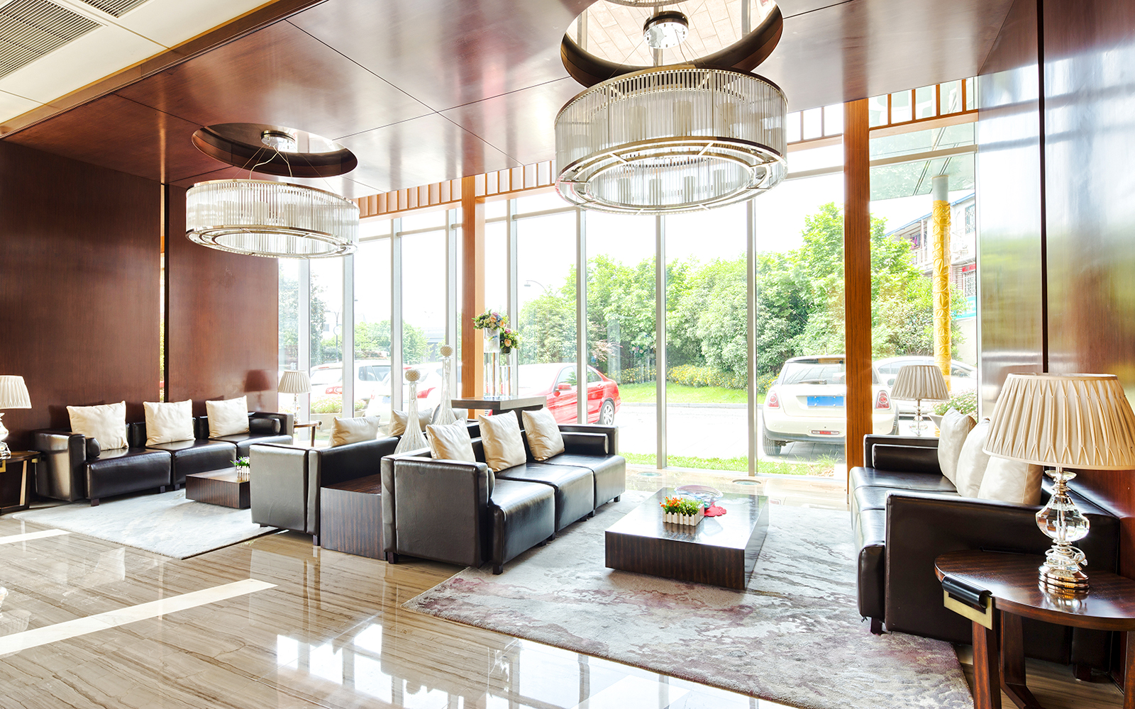 Modern hotel reception with leather sofas, large windows, and elegant chandeliers.